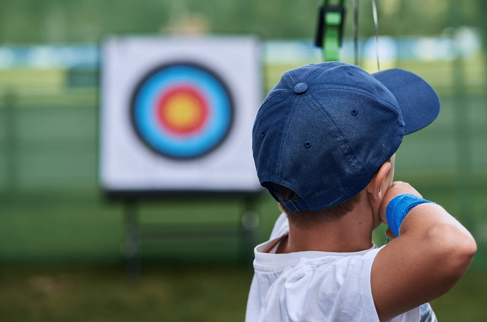 A child wearing a blue cap aims a bow and arrow at a target during archery practice at Nirantara Resort & Spa.