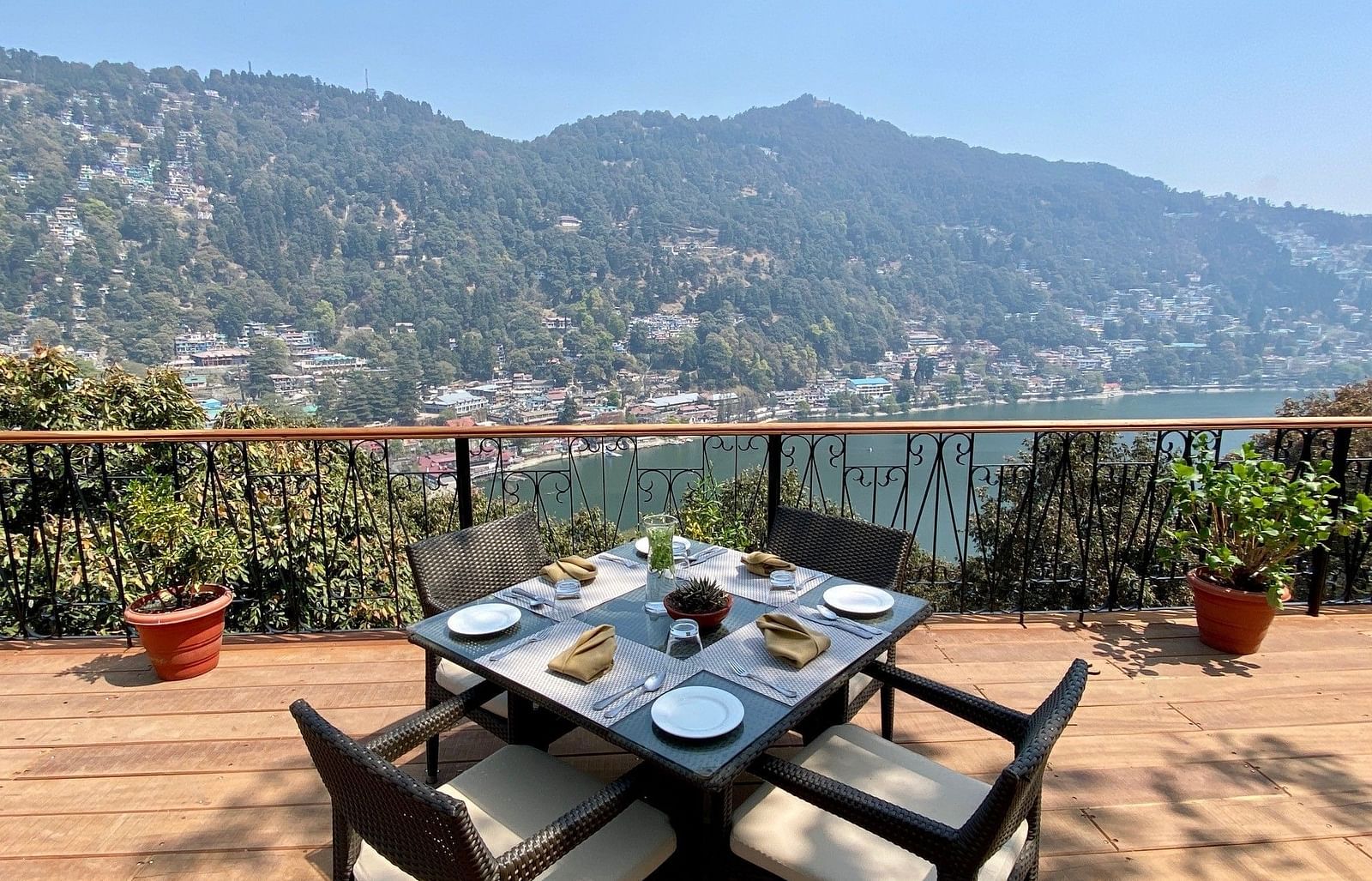 Image showing few chairs placed on the  sides of a square table, pot on either side of the frame, beautifully framed by the backdrop of the mountain ranges.