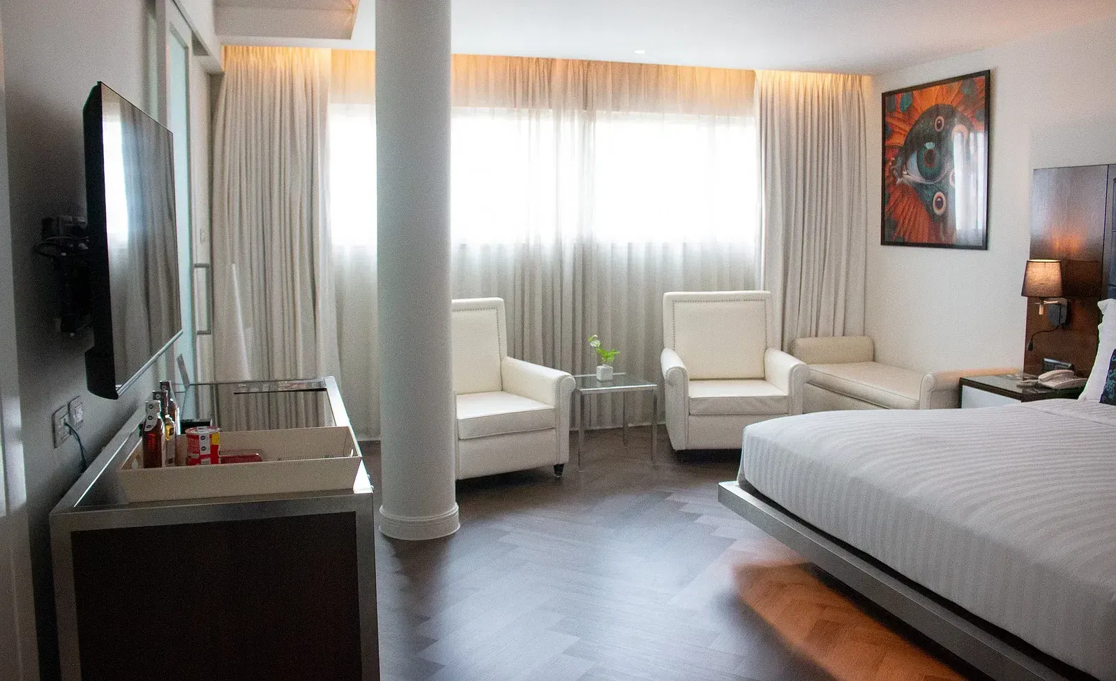 Premium hotel suite with structural column, cream seating area, entertainment console, large windows, and sophisticated neutral colour palette throughout at Night Hotel Bangkok.