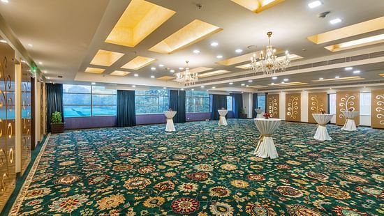 Spacious event hall with a patterned green carpet, elegant chandeliers, and draped cocktail tables - Heritage Village Resorts & Spa.