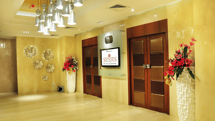 A brightly lit corridor at Senses Hotel with two huge flower vases kept in the corners alongside two wooden doors.