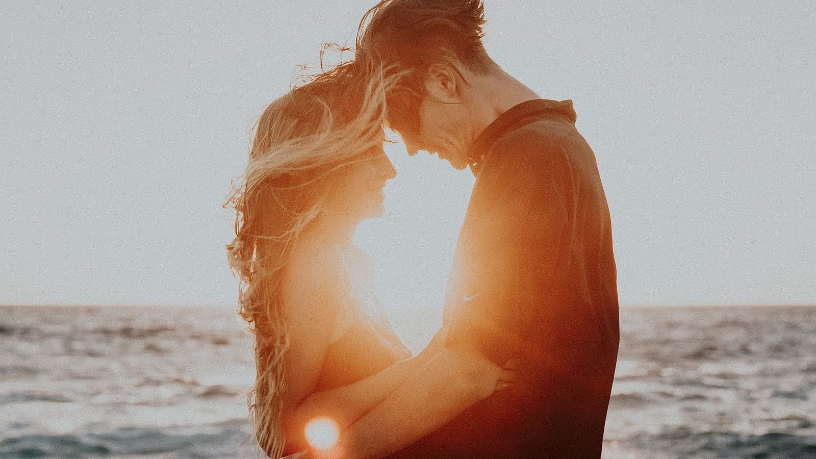 Image of a man and a woman holding each other with a waterbody in the background.