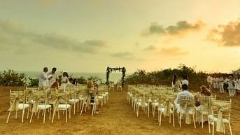 Chairs are set up for an outdoor event, on a sandy area under a dramatic sky at sunset.