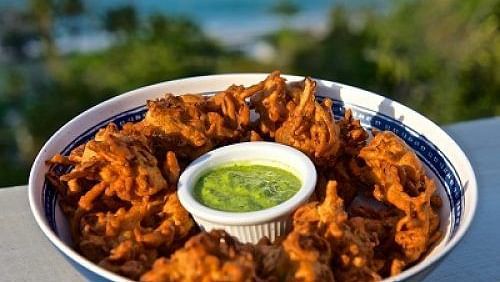 Bowl of fried snacks with green dipping sauce, placed outdoors with a blurred ocean view | A Stone's Throw Away