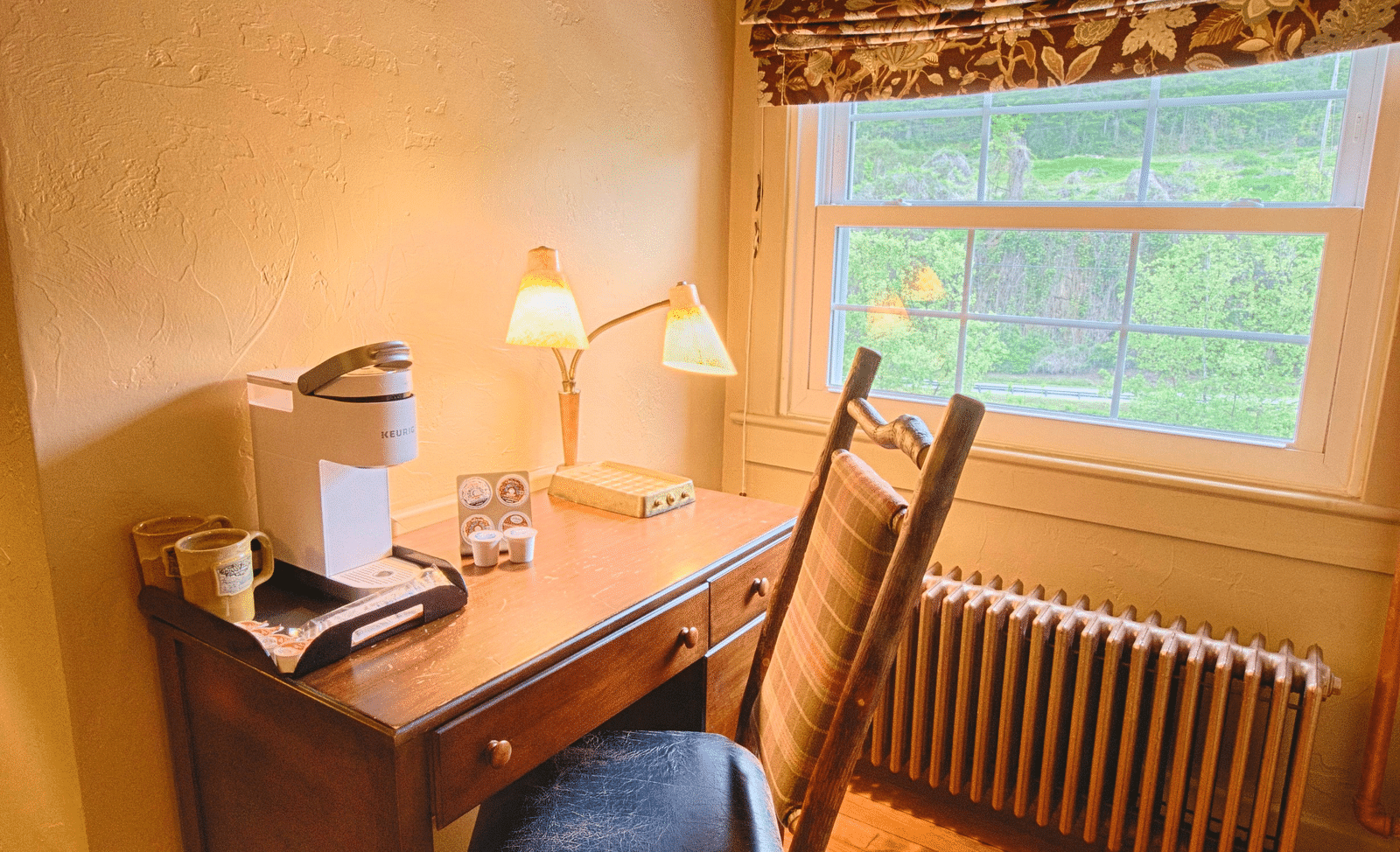 a writing desk and chair along with a table lamp kept besides a window - Historic Tapoco Lodge
