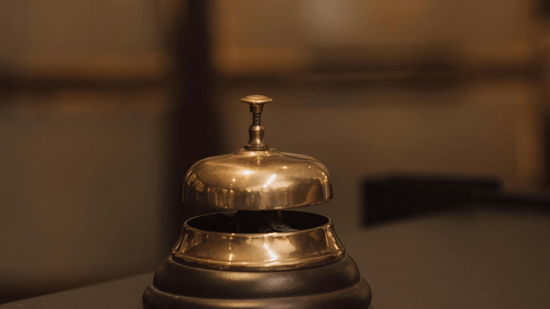 A classic brass service bell placed on a hotel reception counter with a blurred background.