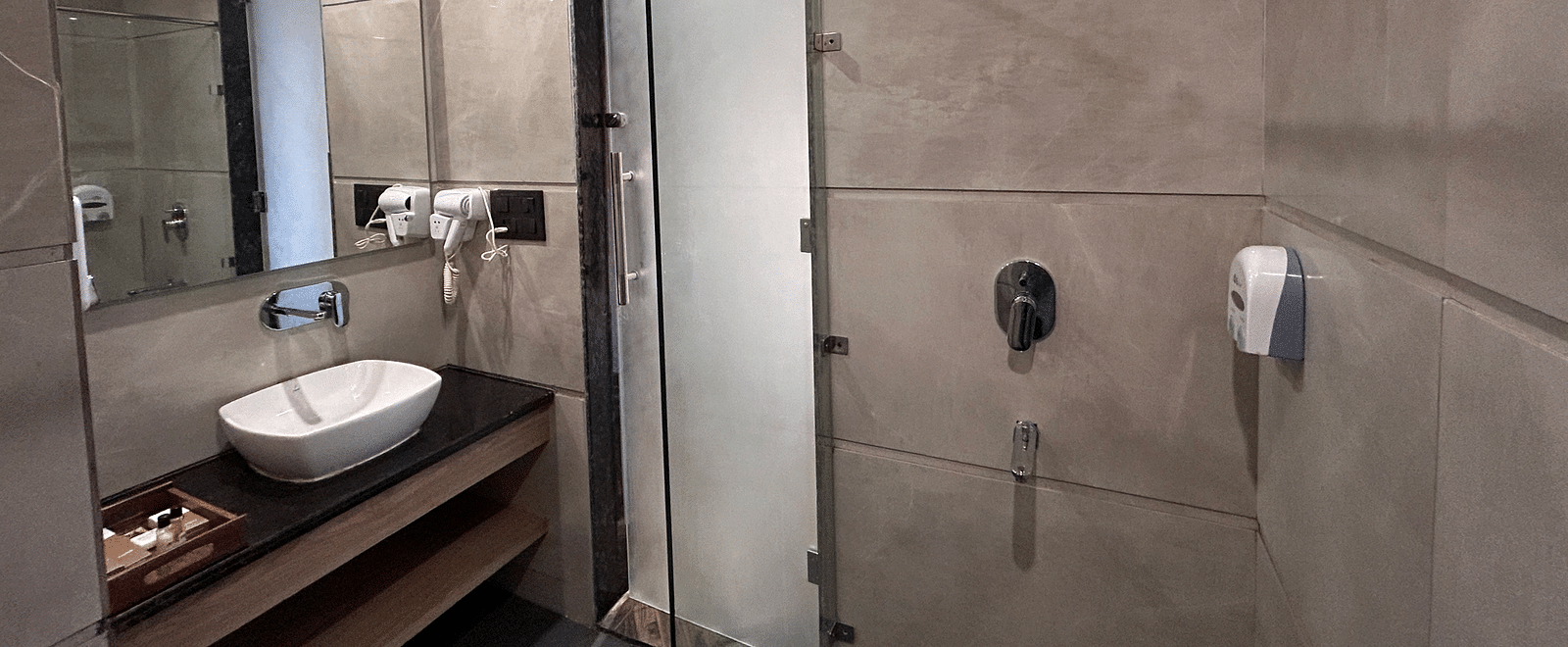 A modern washroom of the deluxe room at DLS Grand Luxotica, Dehradun with a wash basin in front of the huge mirror