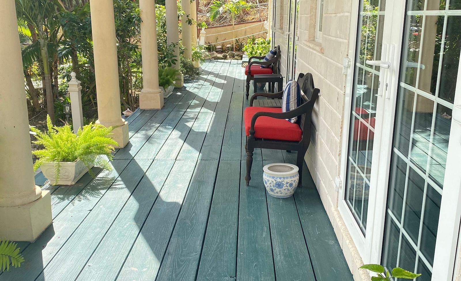 Outdoor walkway with green wooden flooring and red chairs outside a room | A Stone's Throw Away