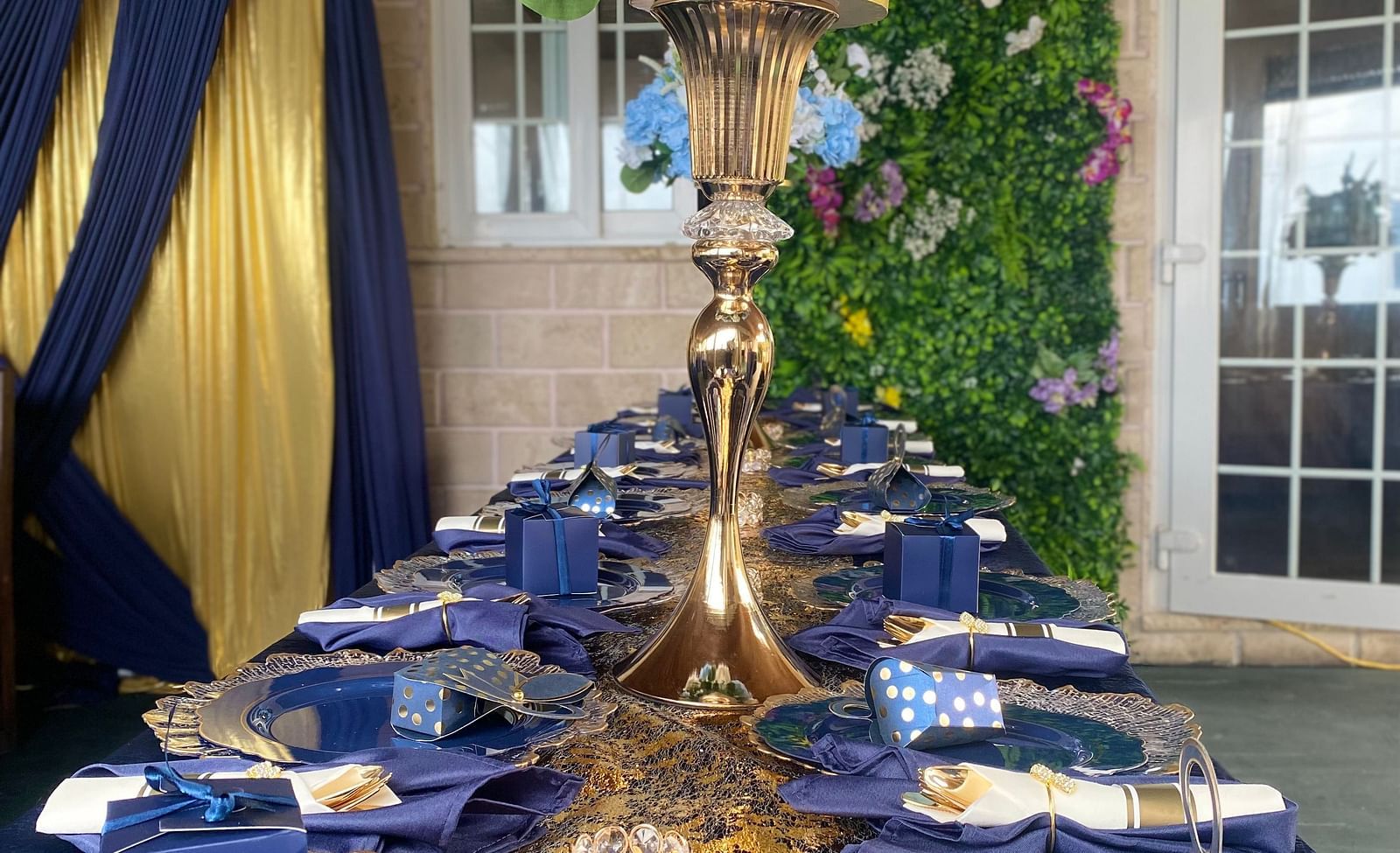 Long banquet table with navy blue napkins, golden cutlery, and tall floral centerpiece | A Stone's Throw Away