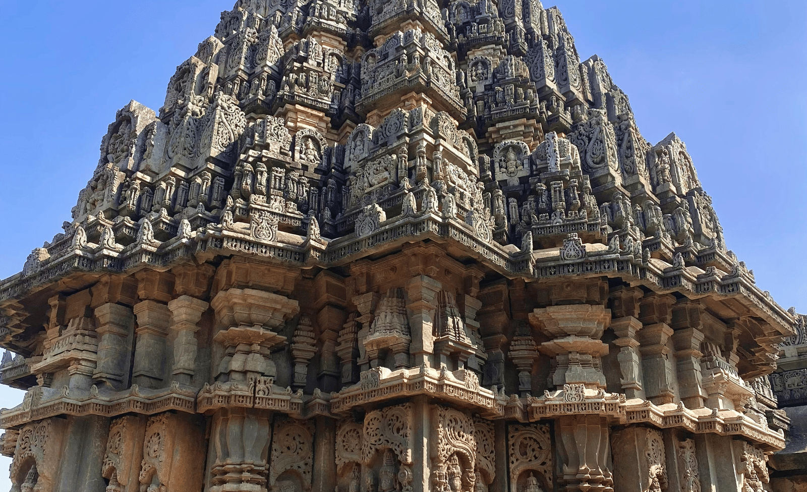 A close-up of an ornate historic Indian temple spire with intricate stone carvings under a clear blue sky.