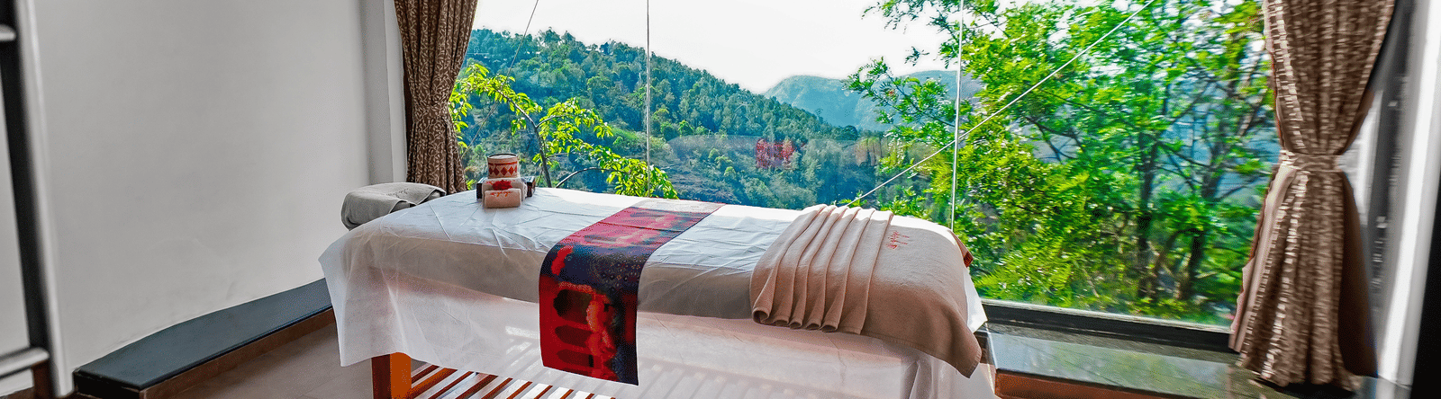 Spa at Grand Palace, Yercaud with bed, wooden floor, curtains, single bed, TV, window, green scenery visible outside the window.