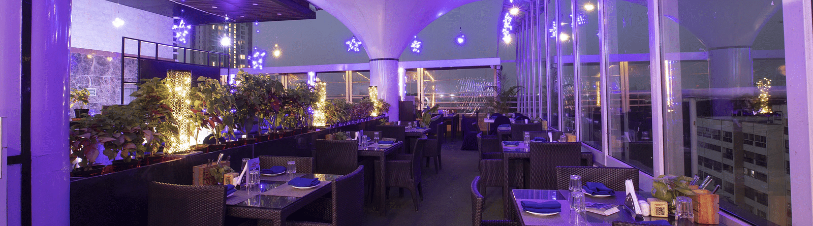 Skylit Rooftop Restaurant with glass walls, ambient purple lighting, neatly arranged tables, and city views, creating a vibrant and upscale dining atmosphere at The Cunningham Hotel