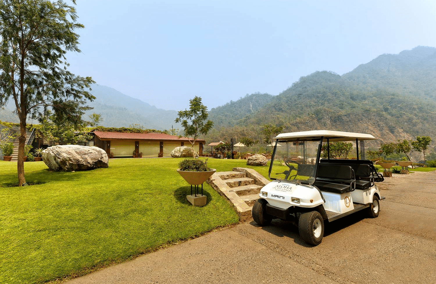 A golf cart parked on a gravel path in a lush landscape in the background and mountains in the distance.