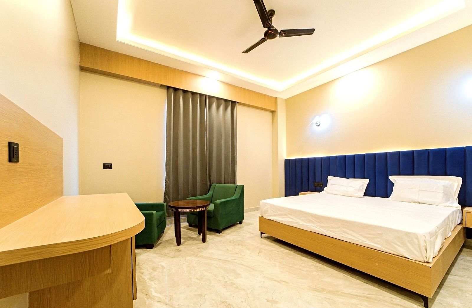 Modern guest room at Grassfield Riveria Resort, Jaipur, featuring a large bed, seating area, ceiling fan, and warm lighting.