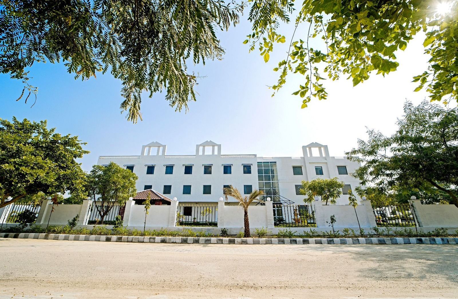 Front view of Grassfield Riveria Resort, Jaipur, surrounded by trees and clear skies, showcasing the modern building facade.