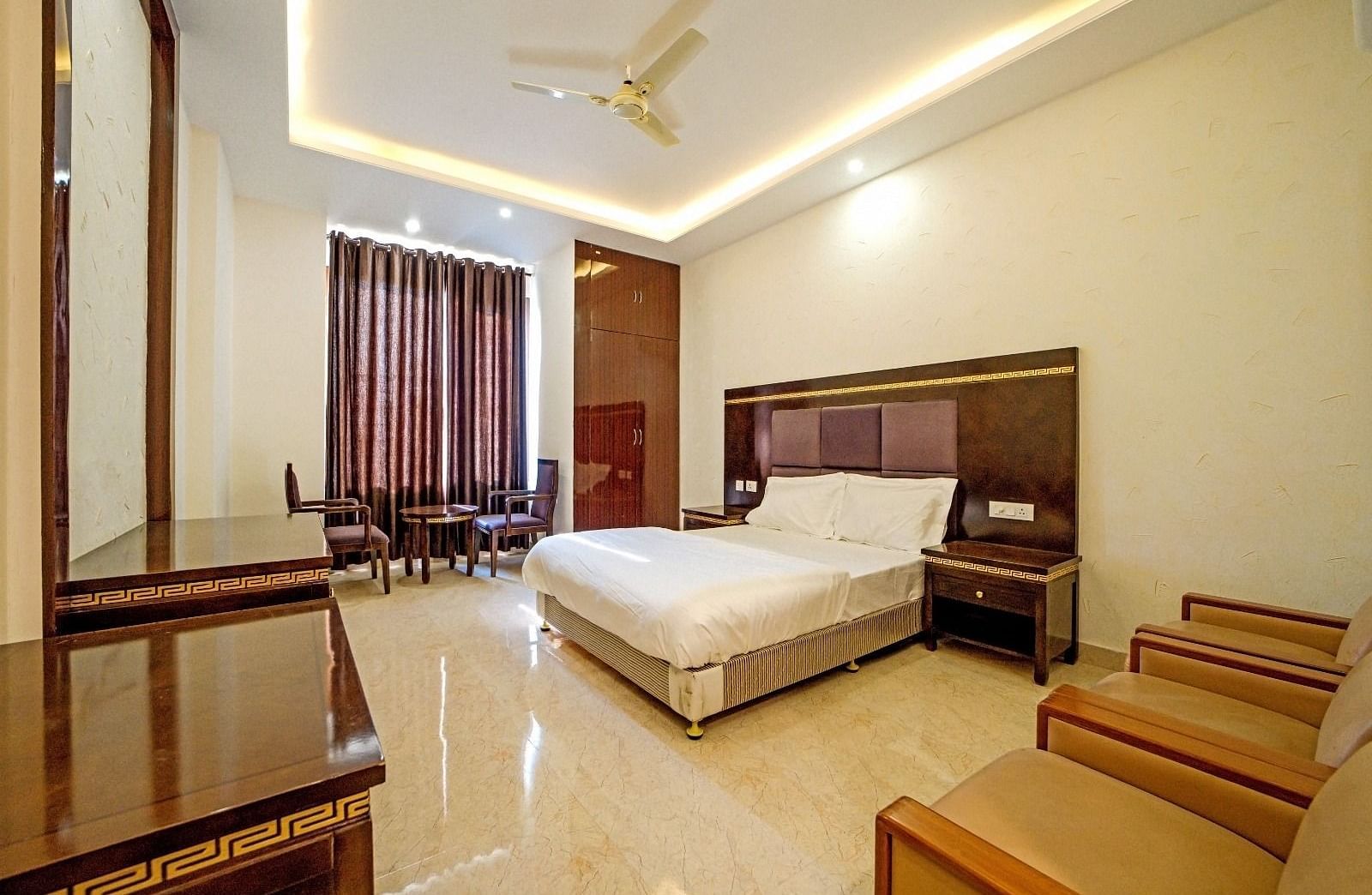 Elegant bedroom at Grassfield Riveria Resort, Jaipur, featuring a large bed, wooden furniture, and warm ambient lighting.
