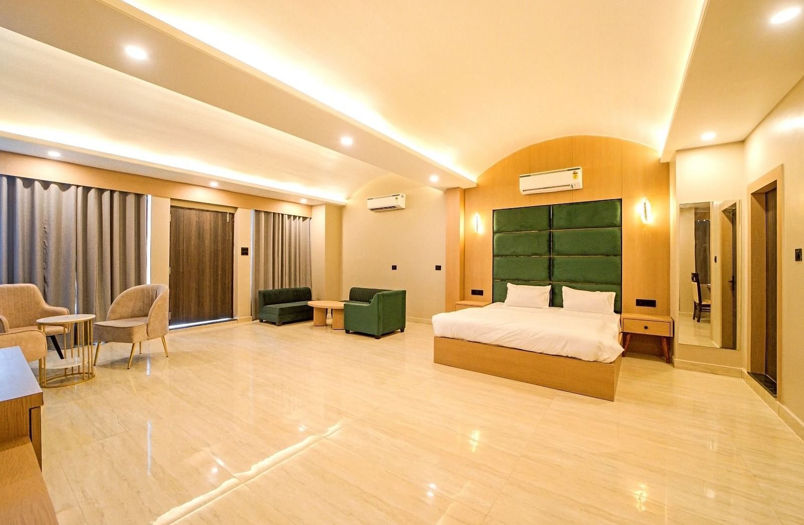 Spacious bedroom at Grassfield Riveria Resort, Jaipur, featuring a large bed, seating area, modern lighting, and floor-to-ceiling curtains.