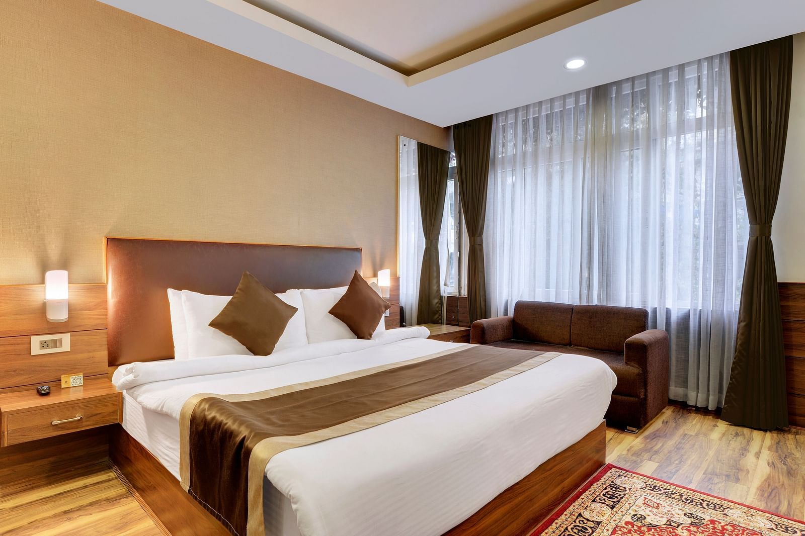 An image of a room featuring a bed, bed side tables, lapms, a rug, and a sofa - Yashshree Hotels