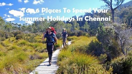 Two people walking on a pathway surrounded by grass and trees, with the text '10 Places To Spend Your Summer Holidays In Chennai' on the image.