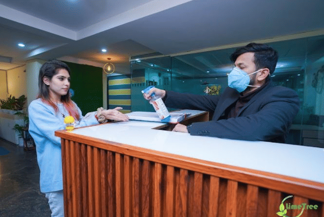 Staff at the wooden reception counter assisting a guest at Lime Tree Hotel Near 32nd Avenue, Gurgaon