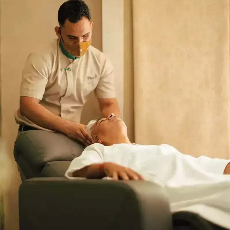 Male spa therapist giving a facial massage to a client lying on a treatment chair, in a softly lit room at Karma Chalets.