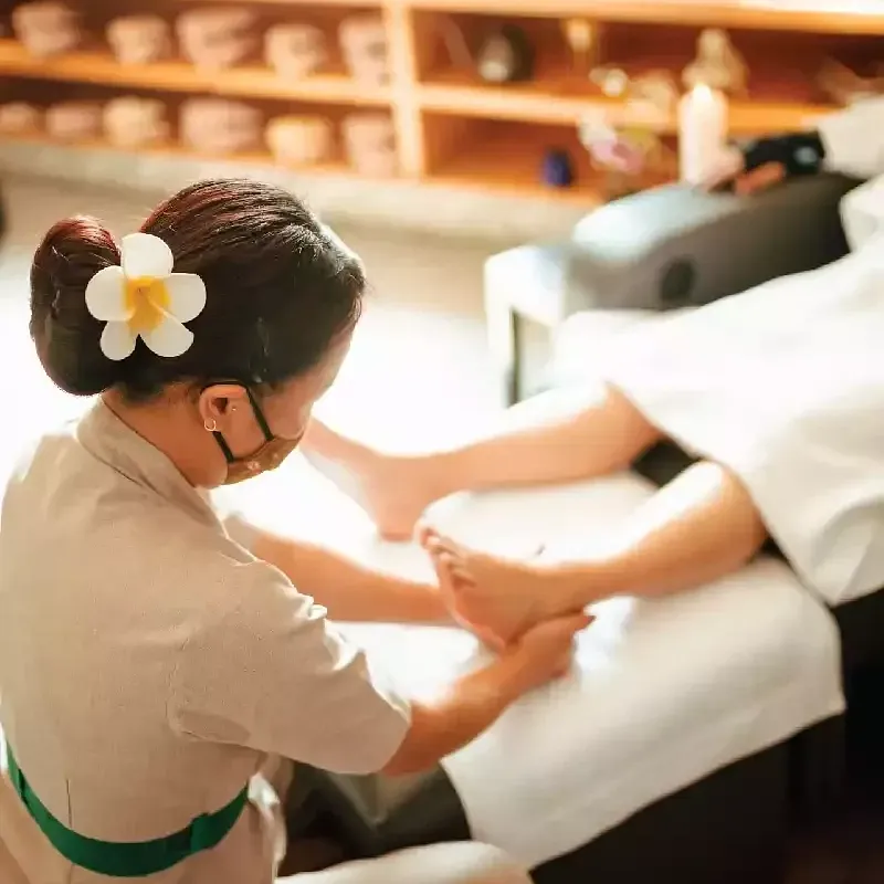 Spa therapist giving a leg massage to a client lying on a white massage bed with wooden shelves in the background at Karma Chalets.