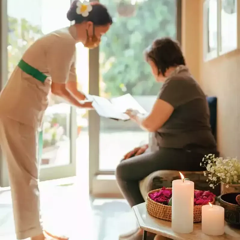 Spa therapist offering a foot treatment to a seated woman by a window, with candles and spa items nearby. at Karma Chalets