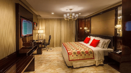 Presidential Suite bedroom at Samanvay Luxury Boutique Hotel, Udupi with a king-size bed, red cushions, a chandelier, a desk, and marble flooring.
