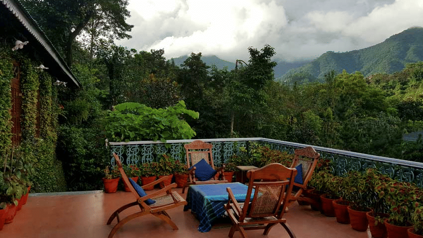 An outdoor seating space at Shaheen Bagh - A Luxury Boutique Resort & Spa in Dehradun, featuring 4 chairs surrounding a table on a balcony with the backdrop of mountains and trees