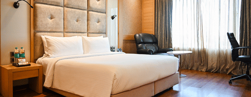 A well-appointed hotel room with a large bed, wooden headboard, and elegant furnishings, suggesting comfort and luxury.