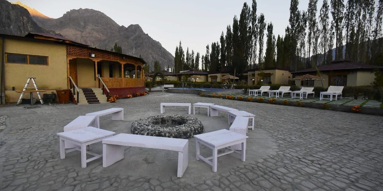 A bonfire setting with white seating area surrounded by buildings at White Sands Resort, Ladakh.