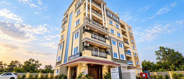 Front view of the Value Inn, Bangalore Airport building at sunset with its cream and yellow facade, ornate balconies, hotel signage, and wooden entrance doors