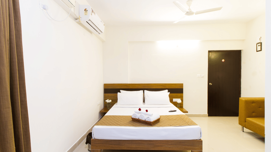 Hotel room with a double bed, an air conditioner, a ceiling fan, and a sofa at Sanctum Suites Whitefield, Bangalore.