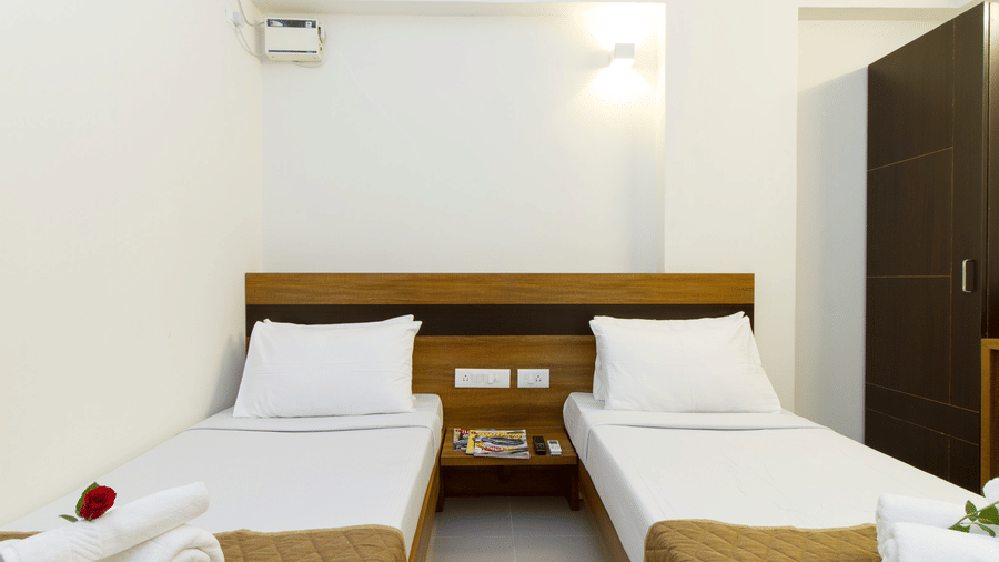Twin bedroom with two beds, wooden headboards, an air conditioner, and folded towel arrangements at Sanctum Suites Whitefield, Bangalore.