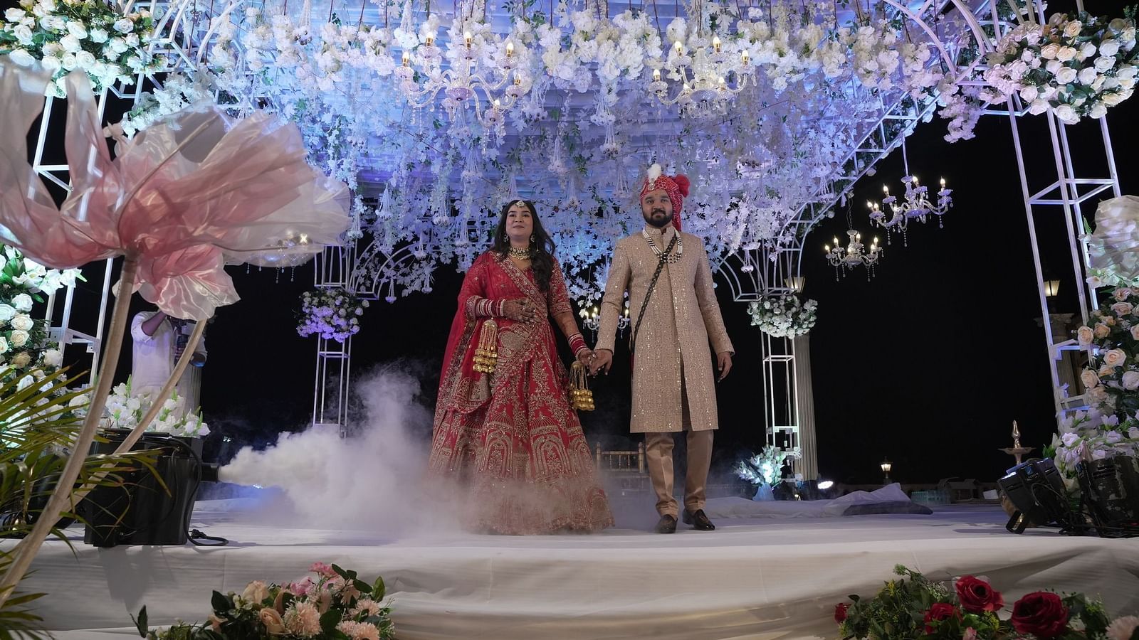 Bride and groom holding hands on the stage which is decorated with flowers at The Grand Legacy Resort & Spa