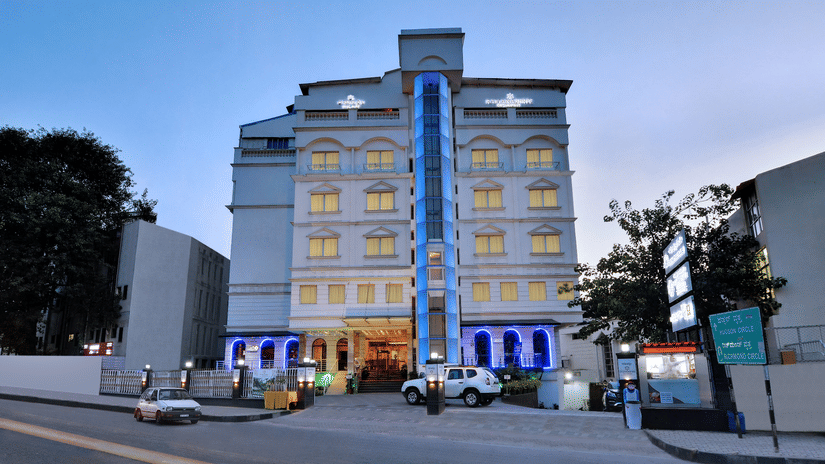 Hotel building exterior with entrance, parked cars, and lights in the evening.