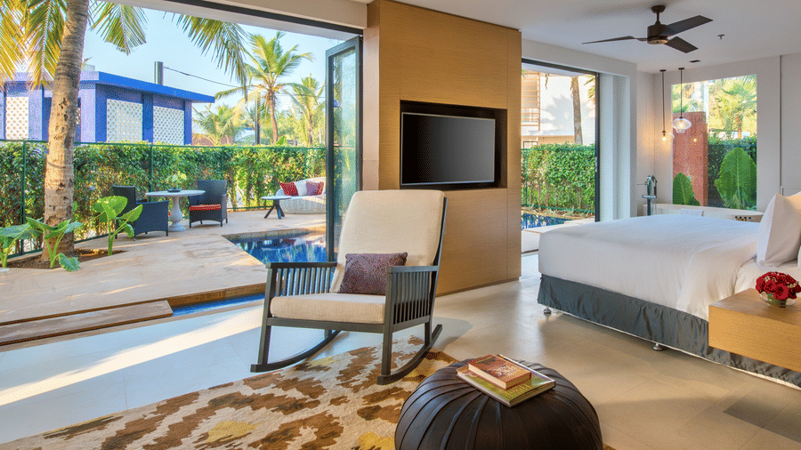 Luxurious poolside room with large glass doors, tropical garden views, cosy seating area, and a spacious bed for a relaxing stay at Azaya Beach Resort Goa