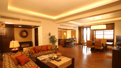 A hotel suite with sofas, tables, chairs, and warm lighting in the living area.