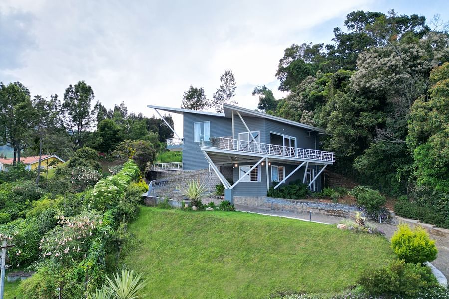 Front view of a contemporary house situated on a grassy hill with trees in the background at Ibex Resorts, Coonoor (Tapas).