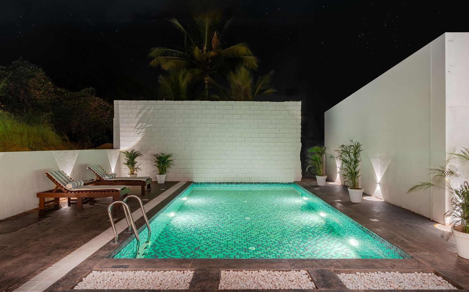 Outdoor pool area with green lighting and privacy walls at night at Bedzzz Xclusiv Morjim, Goa