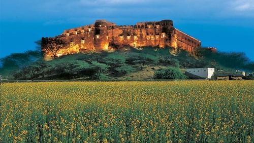 The facade of Hill Fort Kesroli Kesroli with grass at the forefront and blue sky in the background.