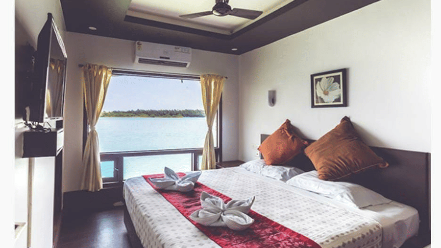Bedroom with a queen bed, brown pillows, ceiling fan, and window view at Paradise Lagoon Resort, Udupi.