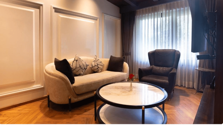 A living area with a white sofa, a black armchair, and a circular coffee table on wooden flooring | Lawrence Solitaire Resort, Nainital