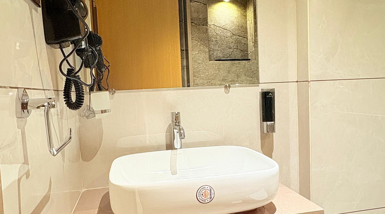 Interior view of a bathroom featuring a wash basin, mirror, and wall-mounted hair dryer at Hotel Mumbai House, Vashi