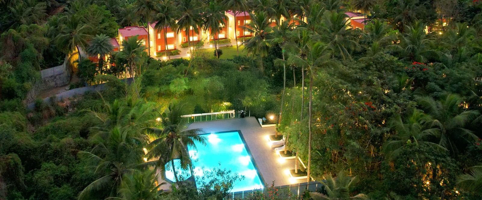 Aerial view of a Mango Hill Resort, Coimbatore with a swimming pool nestled amidst lush greenery and mountains at sunset.