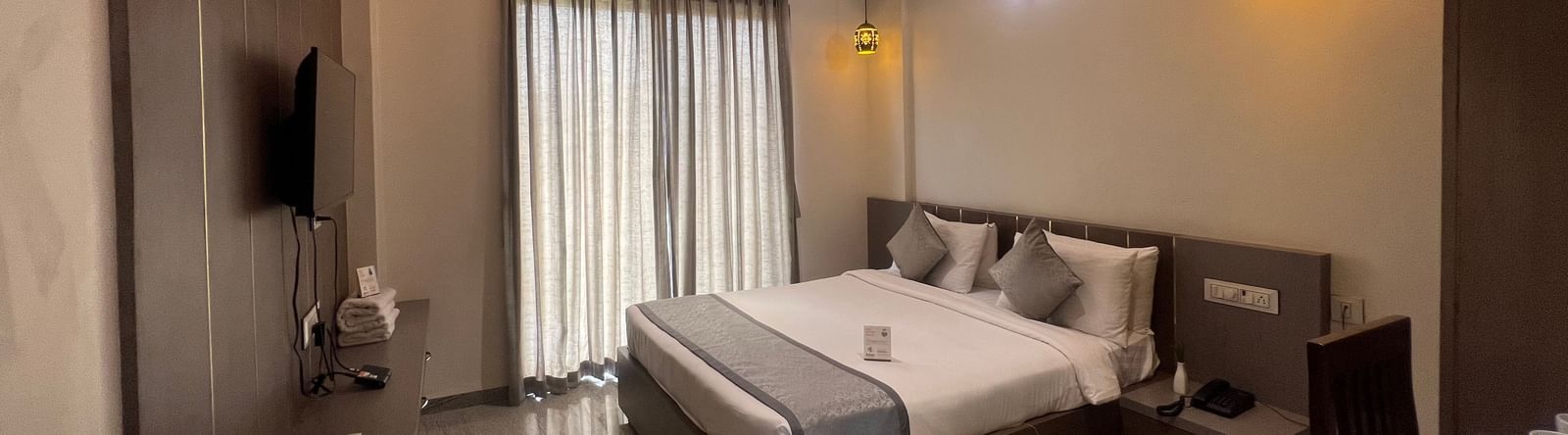 Wide view of the Daksh Bliss room at Daksh The Valley Resort, Saputara, featuring its queen size bed, closed curtains, and designer ceiling.