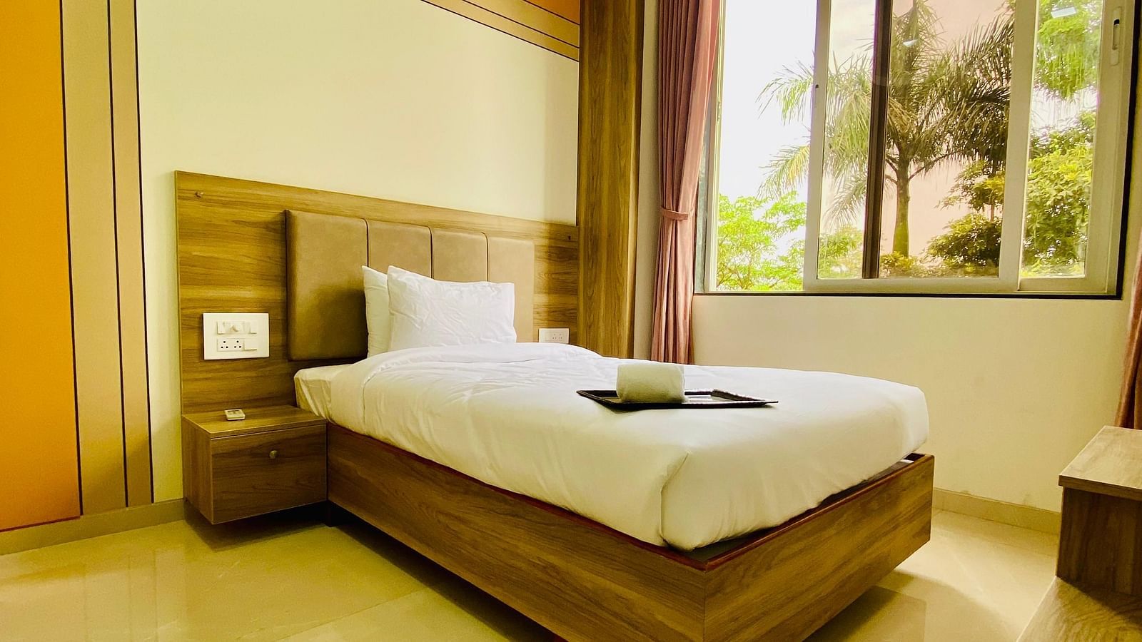 A bright hotel room featuring a neatly made bed, large windows, and a peaceful view of the outdoors.