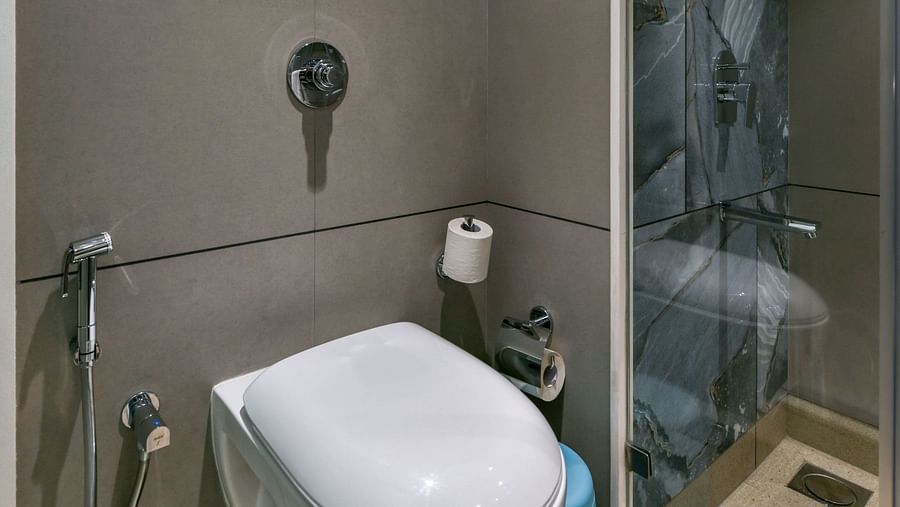 A washroom featuring a western toilet and a shower area separated by a glass panel, at Indie Stays, BKC Kalina.