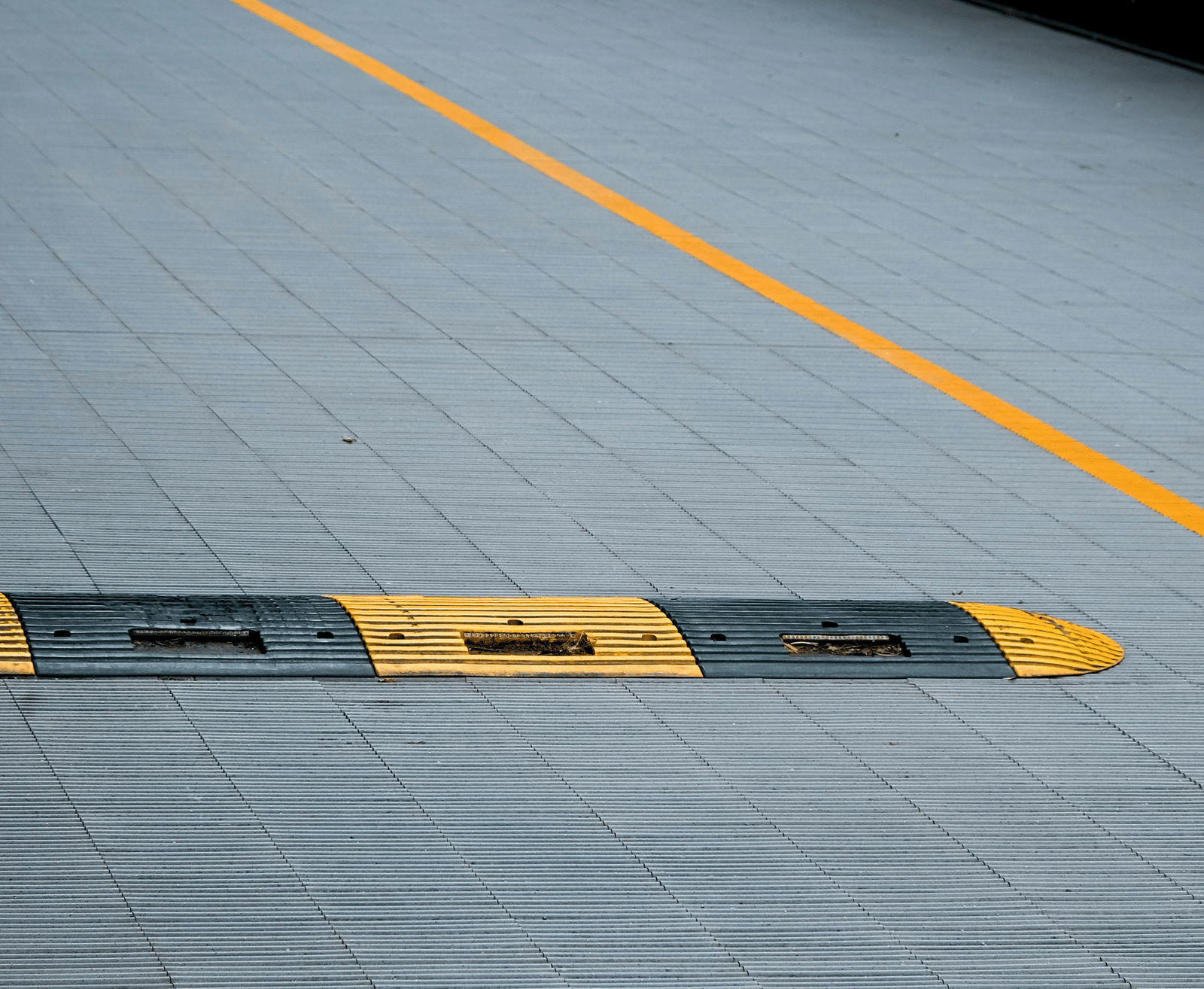 Two yellow and black striped traffic speed humps (sleeping policemen) on a grey asphalt road with a yellow centre line.