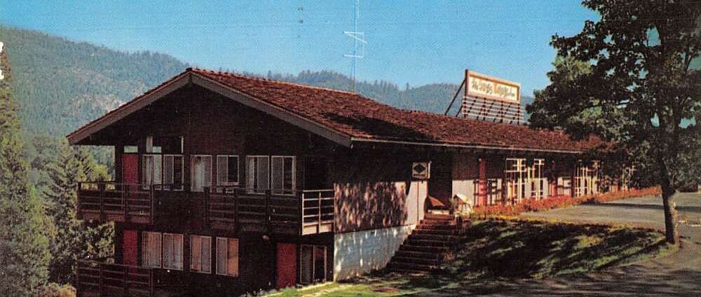 A view of the exterior of Narrow Gauge Inn with the mountains in the far distance on a clear, blue day.